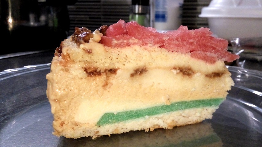 A piece of layer cake with layers of sponges, custards and green and red jelly